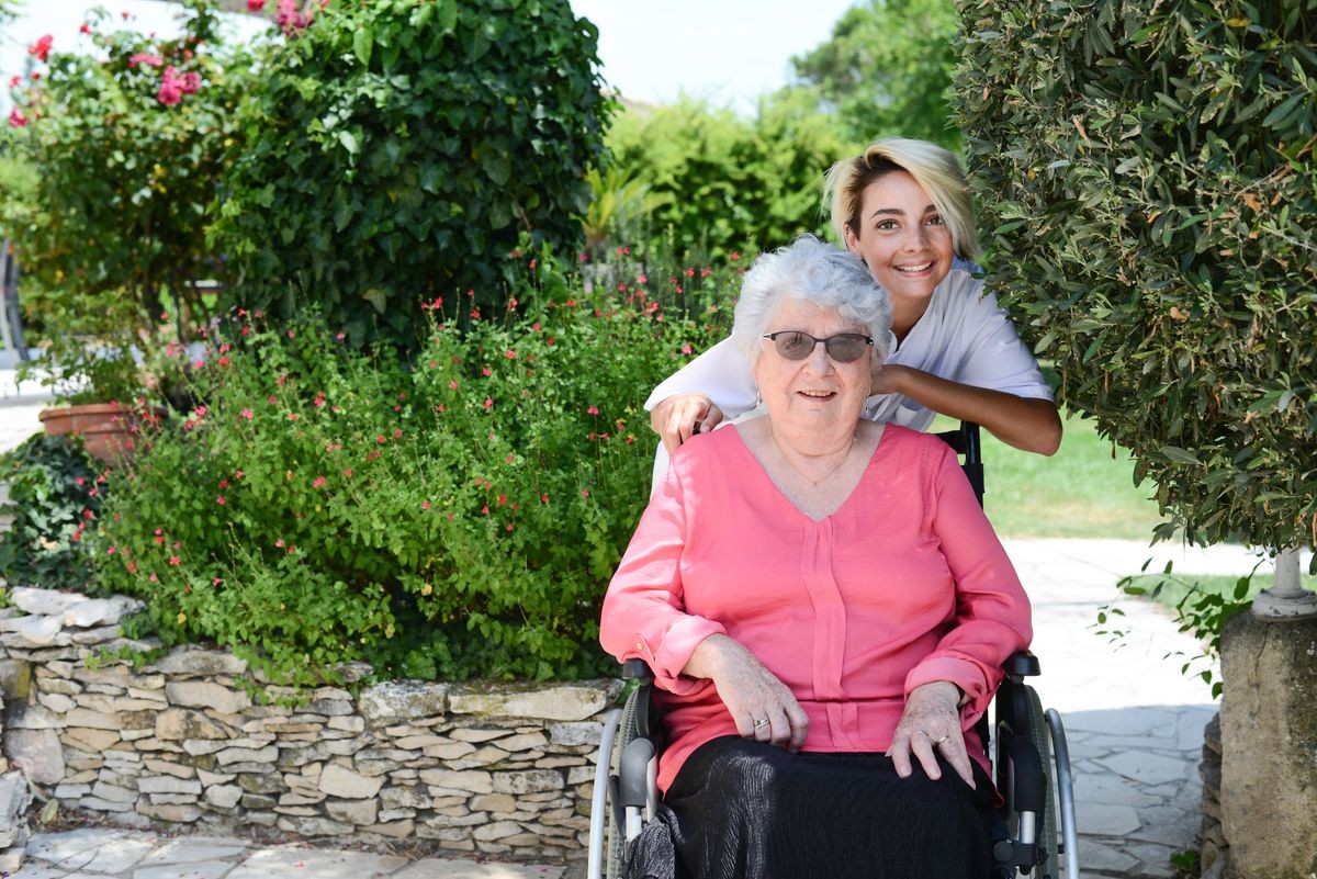 elderly senior woman on a wheelchair with nurse outdoor in nursing home hospital garden